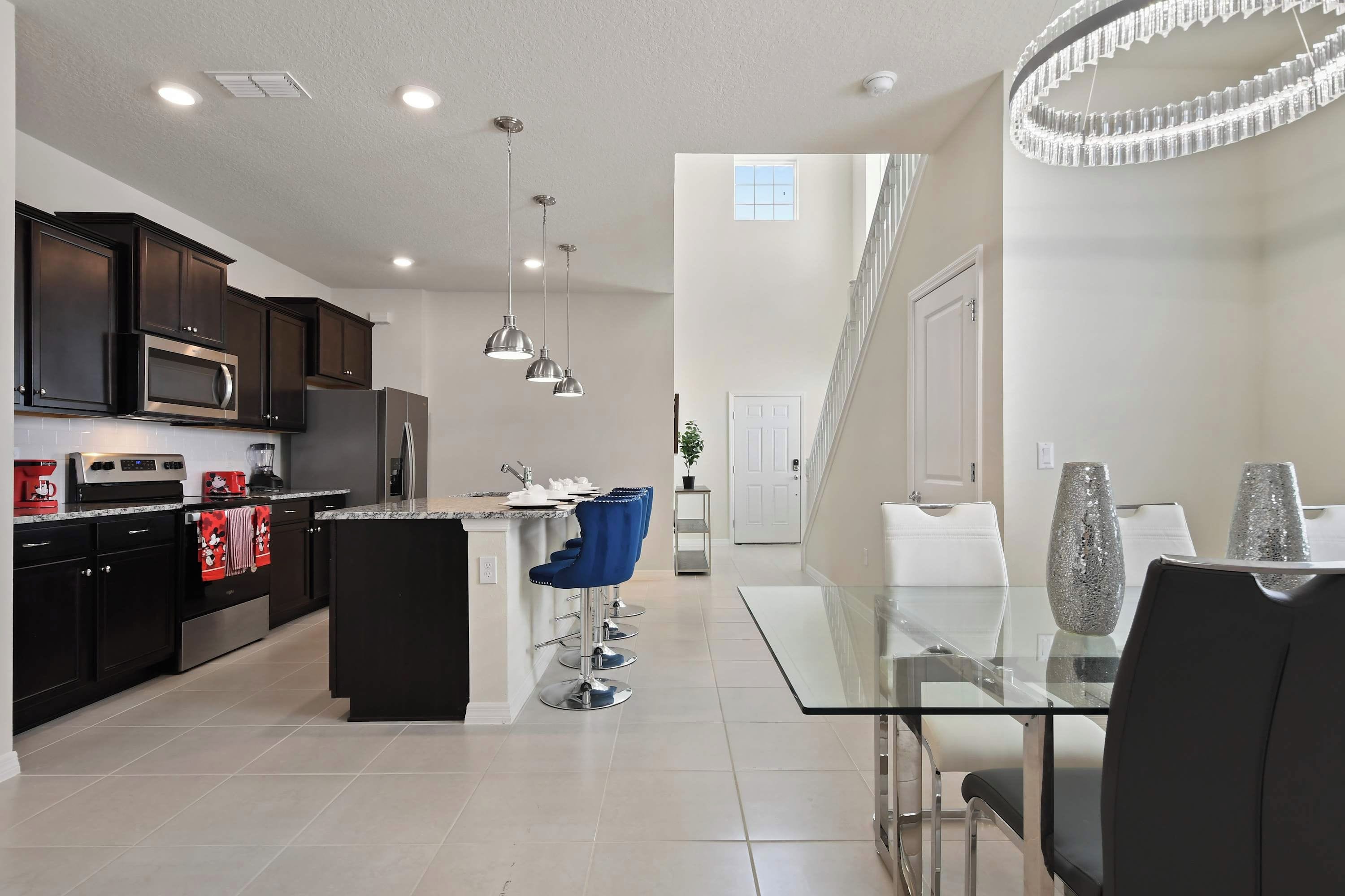 A modern kitchen with dark cabinets, stainless appliances, and a glass dining table with blue bar stools.