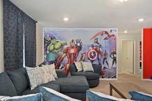 A living room with a large superhero mural, a grey sofa, and a red accent wall. - 6BR Villa w/ Private Pool Near Disney (Davenport)