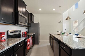 A kitchen with dark cabinets, stainless steel appliances, granite countertops, and pendant lighting. - 6BR Villa w/ Private Pool Near Disney (Davenport)