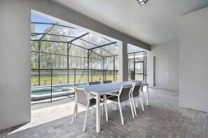 A covered patio with a table and chairs, a swimming pool, and a door. - 6BR Villa w/ Private Pool Near Disney (Davenport)