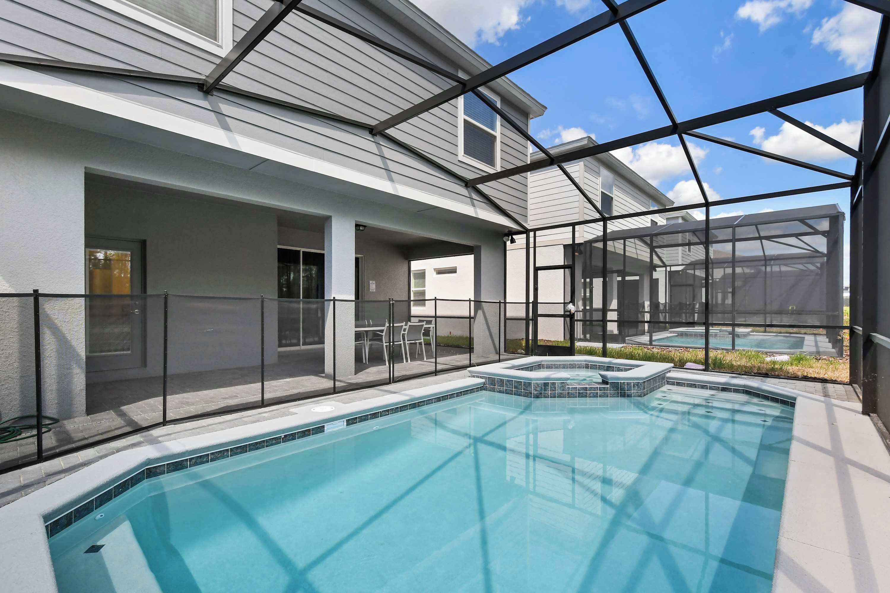 Une piscine dotée d’une enceinte en verre, un jacuzzi et un espace patio aménagé avec du mobilier d’extérieur.