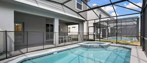 Une piscine dotée d’une enceinte en verre, un jacuzzi et un espace patio aménagé avec du mobilier d’extérieur.