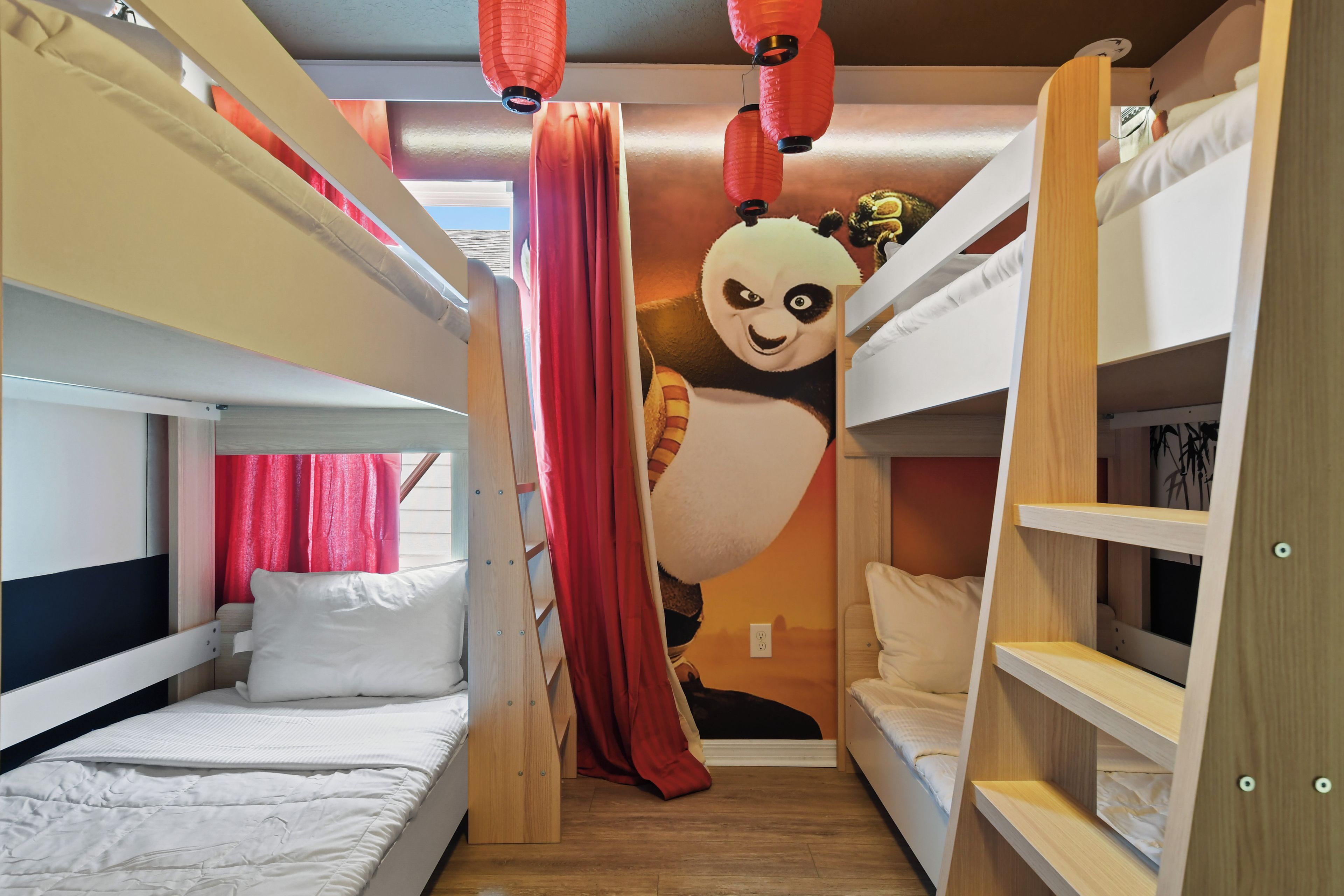 A bunk bed room with a panda mural, red curtains, and wooden shelves.