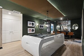 A pool table in a room with a bar area, framed pictures on the wall, and a white door. - Top Gun Bunks + Luxe Bar & Game Room (Davenport)
