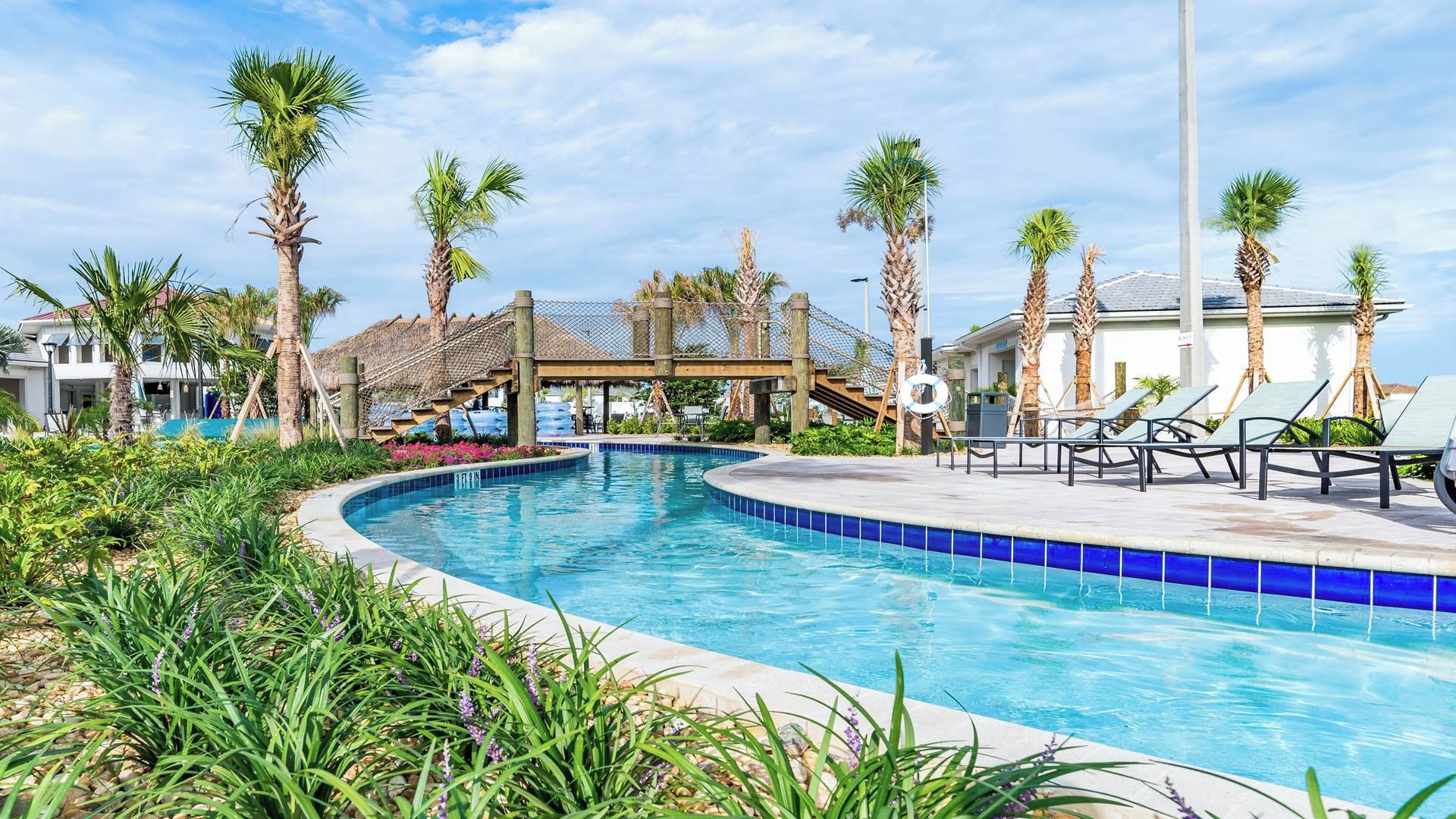 A swimming pool with palm trees, lounge chairs, and a covered area.