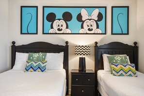 Ein Hotelzimmer mit zwei Betten, jeweils mit Kissen und Kopfteil. Zwischen den Betten befindet sich ein Nachttisch mit Lampe und Schublade.