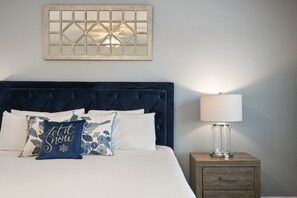 Un lit bien fait, avec une tête de lit sombre, du linge de lit blanc et des coussins décoratifs.