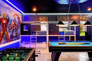 Een kamer met een pooltafel, tafelvoetbal, stapelbedden en een muurschildering van superhelden.