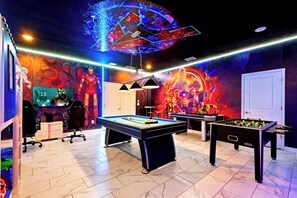 Ein Raum mit Poolbillard, Kicker und einer Spielecke mit großem Bildschirm und Sesseln.