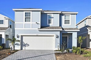 A two-story residential building with a white garage door, a small front porch, and a brick driveway. - Windsor Island Retreat 7BR Pool Home (Davenport)