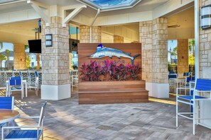 An outdoor seating area with stone pillars, a wooden bench, and a dolphin mural. - Windsor Island Retreat 7BR Pool Home (Davenport)