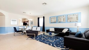 A modern living room with a dining area, featuring a sofa set, a coffee table, and a dining table with chairs. - Game Room, Pool & Themed Bedrooms/close2disney! (Kissimmee)
