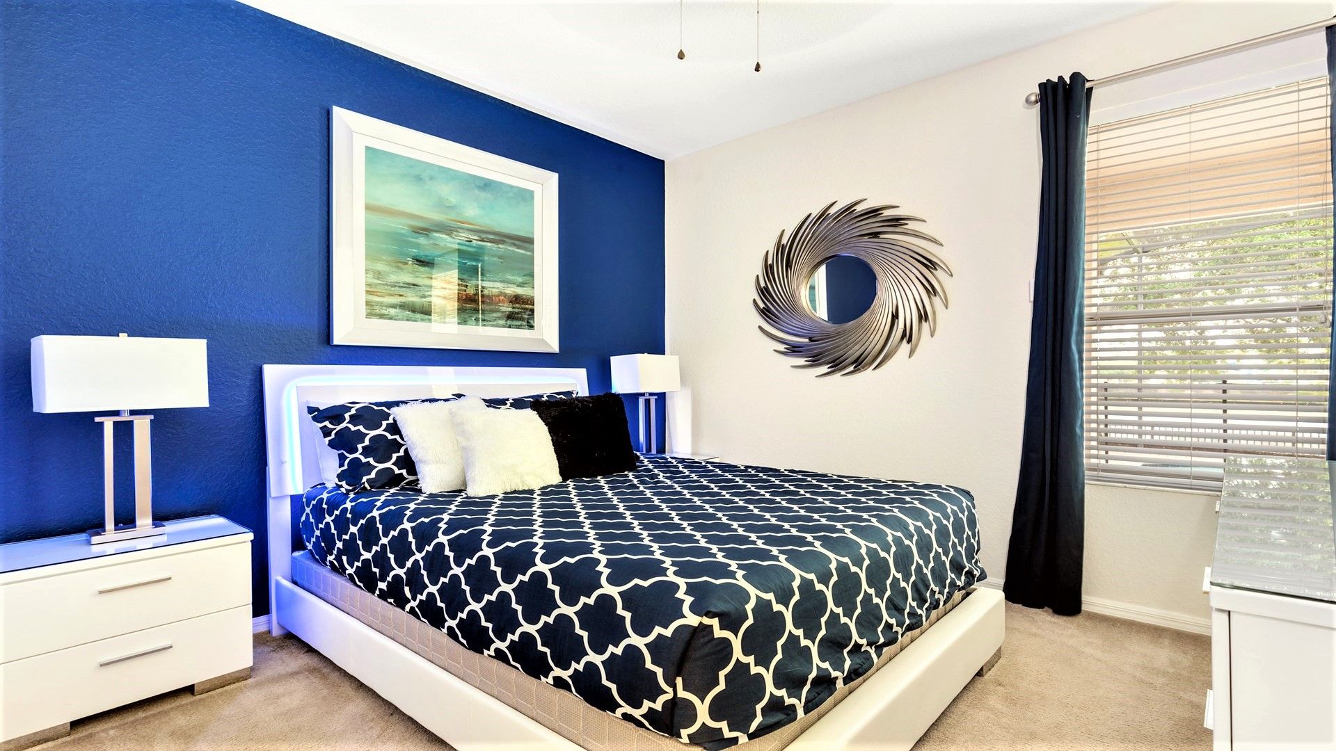 Un dormitorio con cama, mesitas de noche, un espejo en la pared y una ventana con persianas.