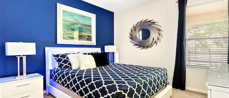 A bedroom with a bed, nightstands, a wall-mounted mirror, and a window with blinds.