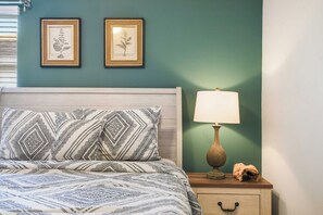Une chambre à coucher avec un lit, deux illustrations botaniques encadrées, une lampe de chevet et un objet décoratif posé sur la table de chevet.
