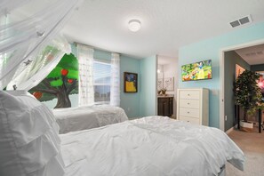 Une chambre avec deux lits, une fenêtre avec des rideaux légers, un luminaire au plafond, un téléviseur fixé au mur et une plante.