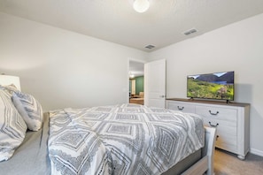 Ein Schlafzimmer mit einem Bett, einem Fernseher auf einer Kommode und einer Tür zu einem anderen Raum.