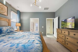 Une chambre à coucher comprenant un lit, une commode, un téléviseur et une porte donnant sur une autre pièce.