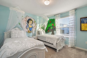 Ein Schlafzimmer mit zwei weißen Betten, einem Nachttisch, einem Wandbild einer Figur und einem Fenster mit Vorhängen.