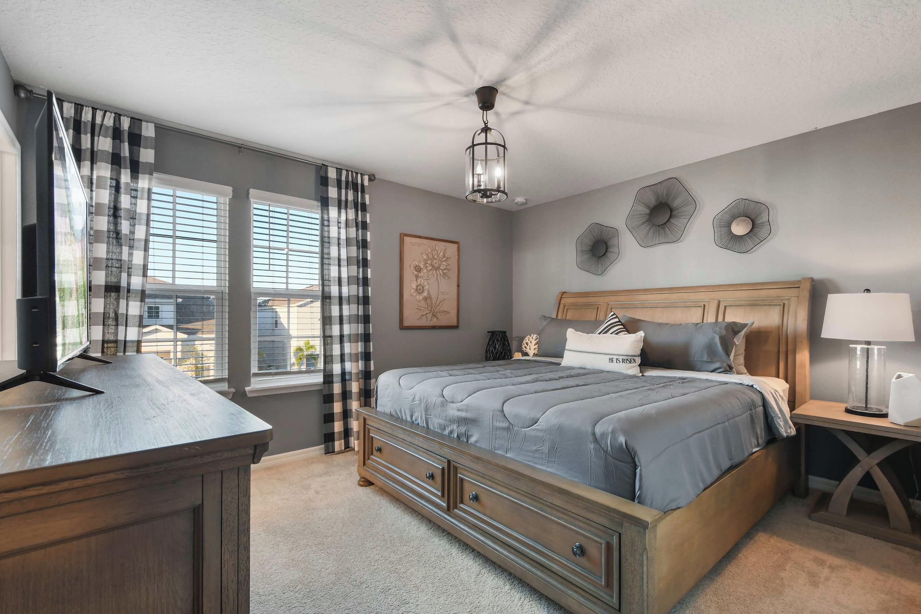 A bedroom with a bed, a bedside table, a lamp, a ceiling light, and a window with curtains.