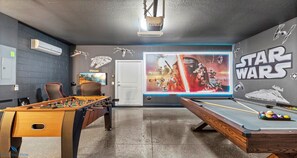 A room with a foosball table, pool table, Star Wars themed wall art, and a projector mounted on the ceiling. - Solterra Resort Gem: Pool, Spa & Disney Decor (Davenport)
