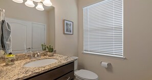 A bathroom with a double sink, a toilet, a window with blinds, a mirror, and a small cactus on the counter. - Solterra Resort Gem: Pool, Spa & Disney Decor (Davenport)