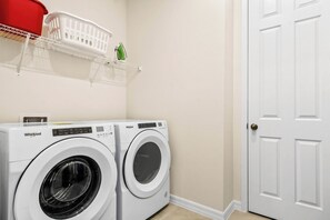 A laundry area with two front-loading Whirlpool washers, a white basket on a shelf, and a white door. - Private Pool Villa With Star Wars & Theater Fun (Kissimmee)
