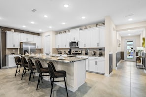 A modern kitchen with white cabinetry, a central island with bar stools, and a breakfast bar. - Private Pool Villa With Star Wars & Theater Fun (Kissimmee)