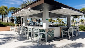 An outdoor bar area with white chairs and a counter, surrounded by a white fence and palm trees. - Private Pool Villa With Star Wars & Theater Fun (Kissimmee)
