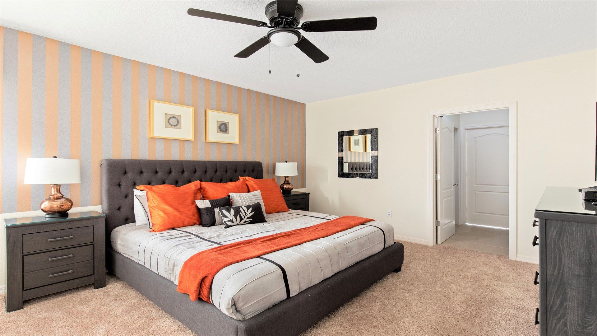 A bedroom with a large bed, two bedside tables, a ceiling fan, and striped wallpaper.