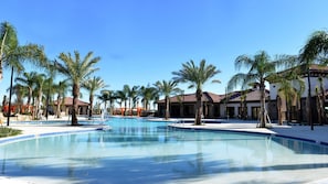 Uma área de piscina de resort com várias piscinas, palmeiras e edifícios com telhados de telha vermelha.
