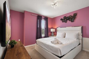 Ein Hotelzimmer mit einem großen Bett, einem Flachbildfernseher, einem Nachttisch aus Holz, einer Topfpflanze und einem Wandbild.