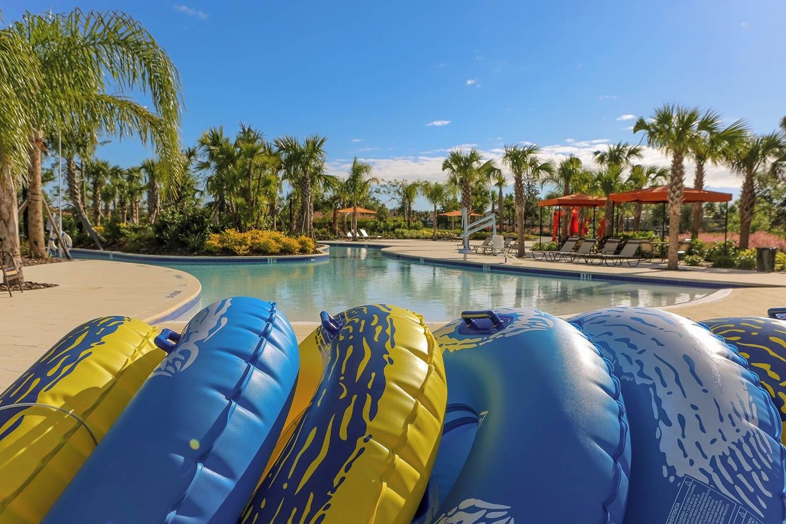 A poolside area with inflatable loungers, palm trees, and lounge chairs under umbrellas.