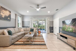A modern living room with a sectional sofa, a coffee table, a flat-screen TV, and a large window with curtains. - Solterra Villa Private Pool, Games & Themes (Davenport)