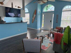 A living room with a flat-screen TV, a dining area with a bench, and a kitchen area with a counter. - Beautiful 3-bedroom house just 1 block from the beach in Panama City Beach (Panama City Beach)