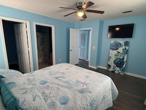 A bedroom with a bed, a ceiling fan, a TV, and a door leading to another room. - Beautiful 3-bedroom house just 1 block from the beach in Panama City Beach (Panama City Beach)