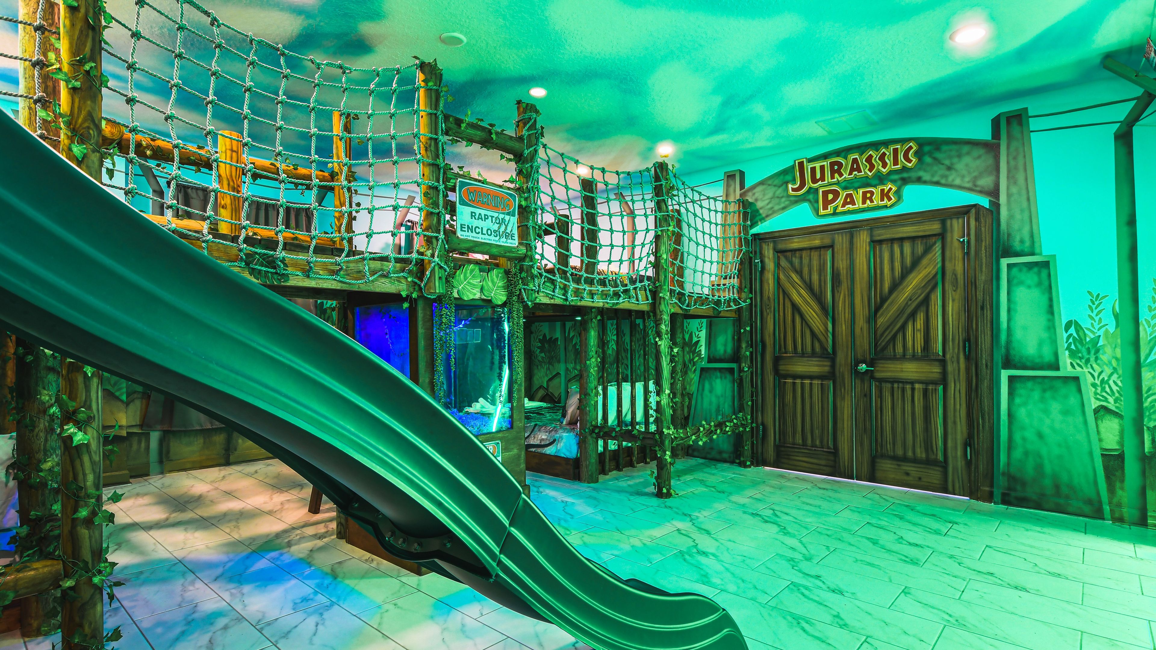 A themed indoor play area with a slide, netted climbing structures, and a sign reading "Jurassic Park".
