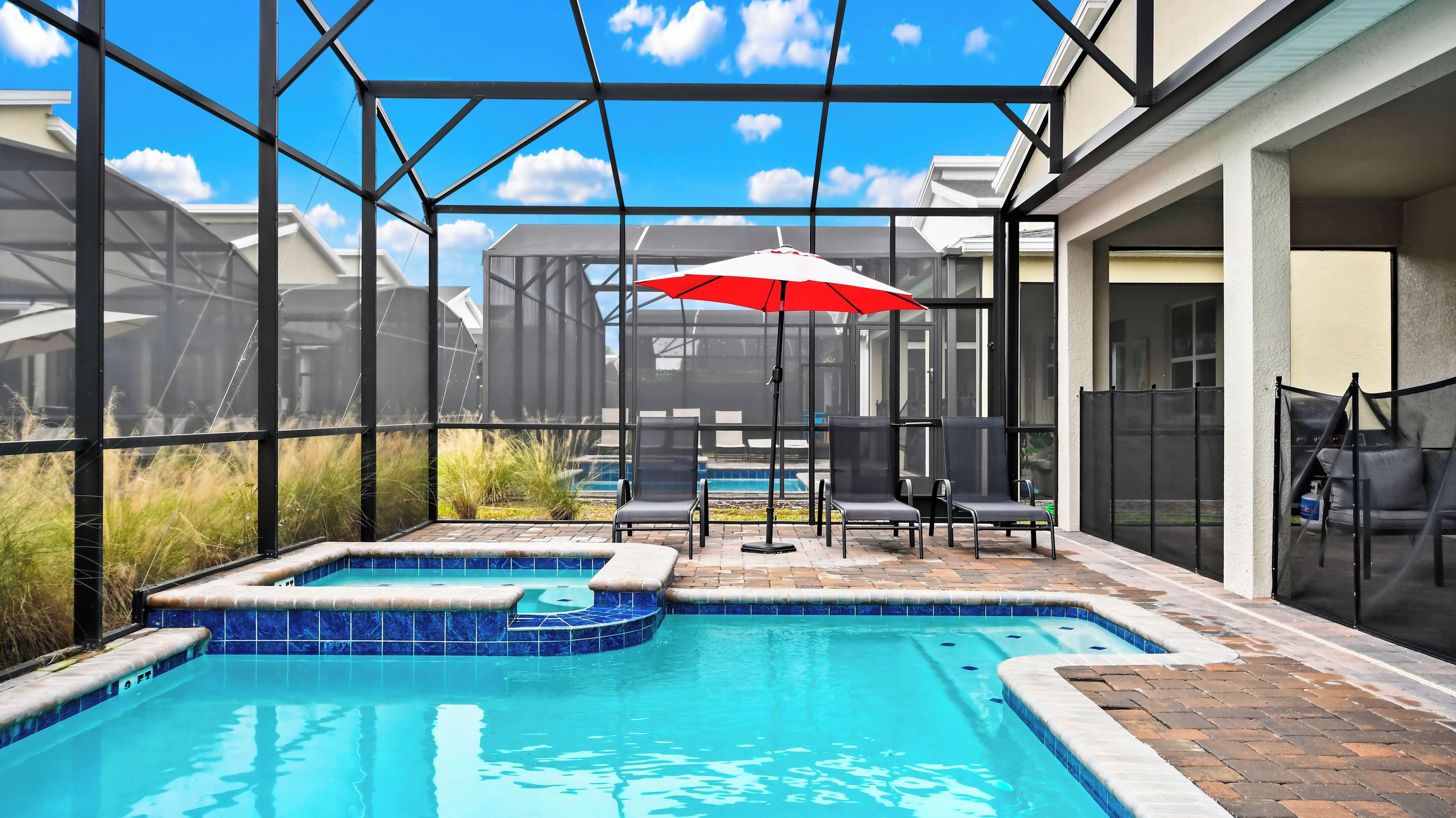 A swimming pool with a hot tub, surrounded by lounge chairs and a red umbrella.