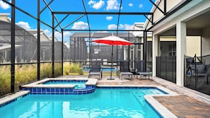 Une piscine avec un jacuzzi, entourée de chaises longues et d’un parasol rouge.