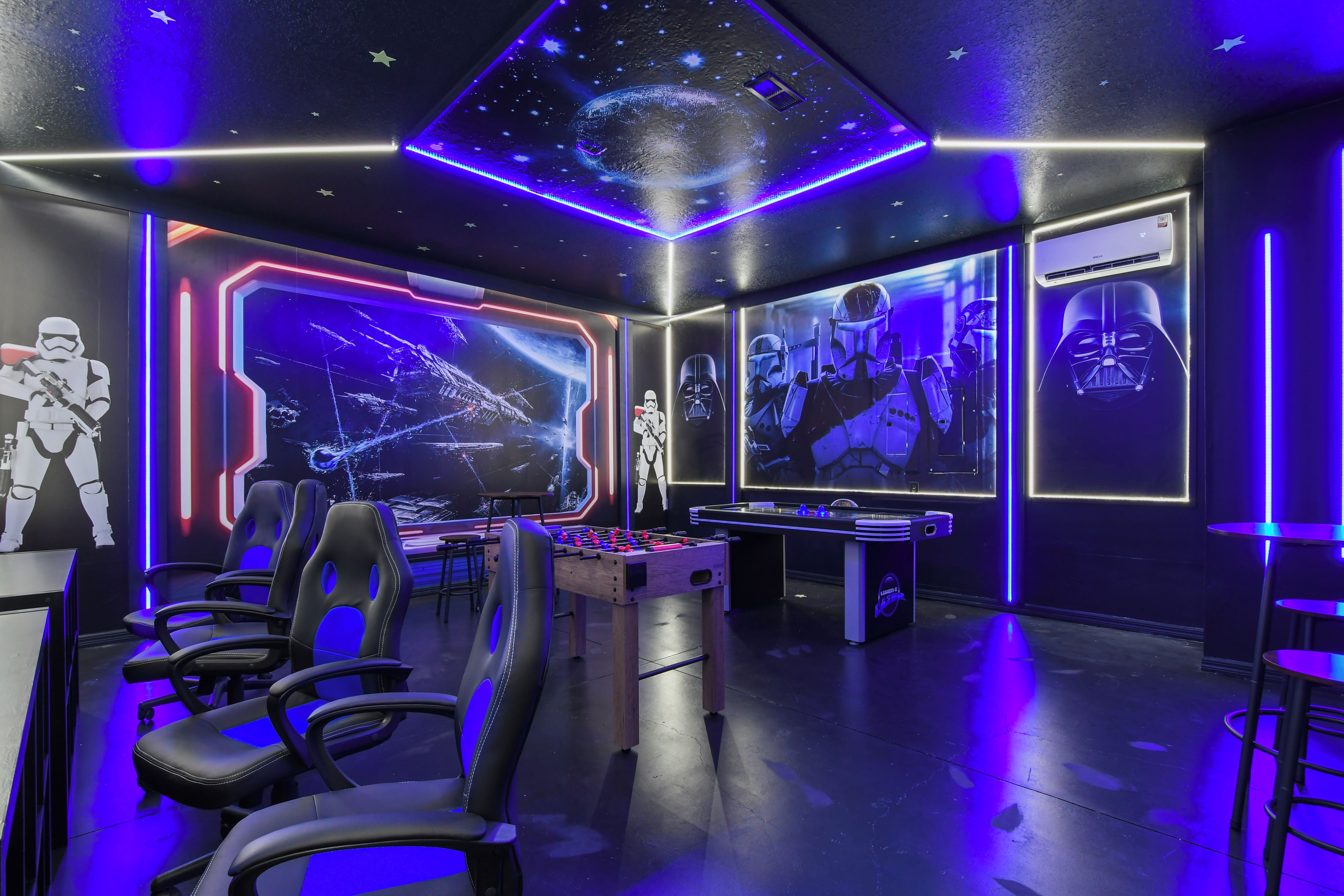 A room with gaming chairs, a foosball table, and Star Wars-themed wall art.