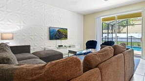 A modern living room with a sofa, a glass coffee table, and a painting on the wall. - 6BR @ Storey Lake w Pool, Themed Room Close2disney (Kissimmee)