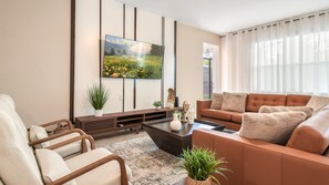 A modern living room with a large flat-screen TV, a brown leather sofa, a wooden coffee table, and a beige armchair. - Star Wars Slide Bunk, Mario/frozen Villa w/ Pool (Kissimmee)