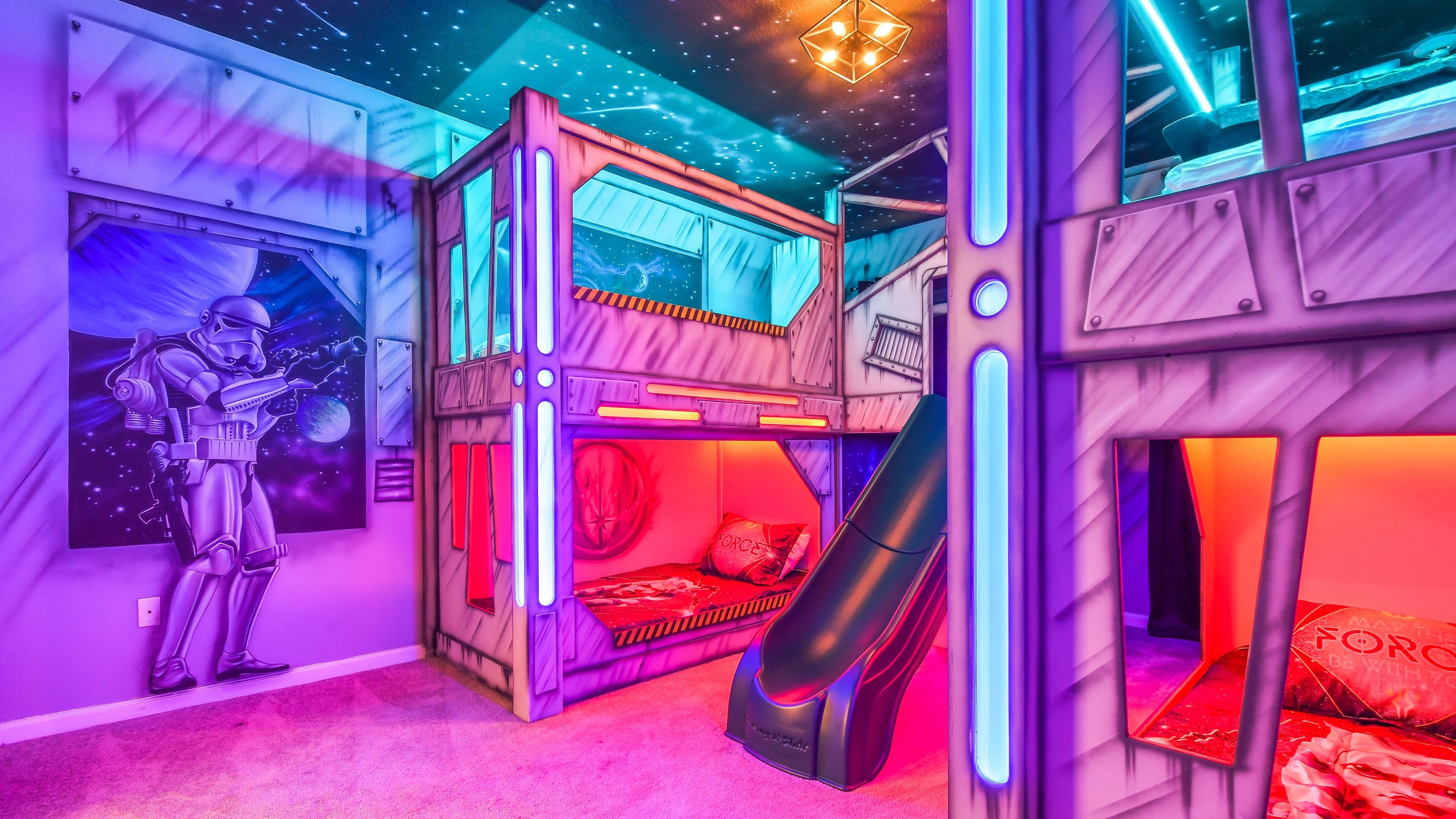 Een slaapkamer met een meerlaags stapelbed, een glijbaan, een muur met Star Wars-thema en een plafond met een sterrenstelselprint.
