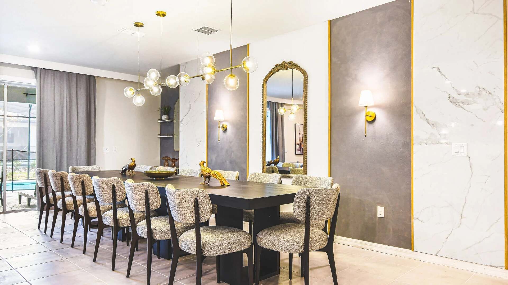 Un comedor moderno con pared de mármol, un espejo grande y una lámpara de araña.
