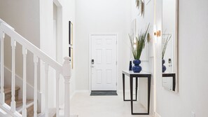Un couloir avec une porte blanche, une console noire sur laquelle est posé un vase, et un miroir accroché au mur.