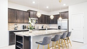 Une cuisine moderne avec des meubles de couleur bois foncé, un grand îlot central doté de tabourets, des appareils en acier inoxydable et un éclairage suspendu.