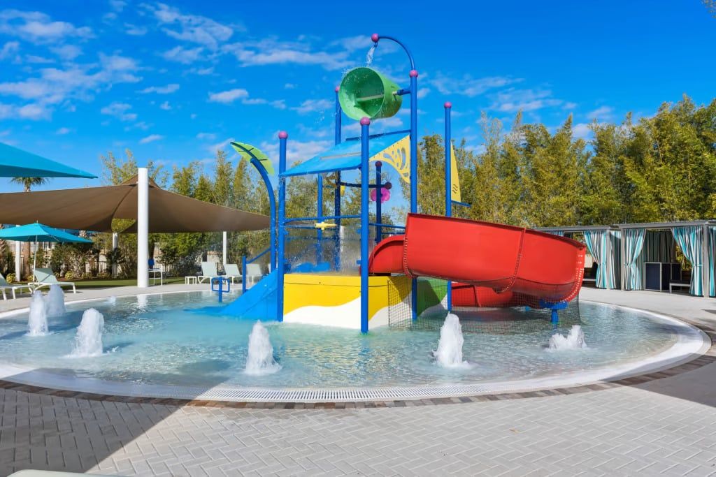 Een water speelplaats met een rode glijbaan, meerdere waterstralen en een blauw-gele speelconstructie.
