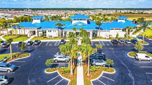 A parking lot with multiple cars, a central landscaped area with trees, and a building with blue roofs in the background. - Vibrant Villa With Tropical Mural & Fun Bunk Beds (Davenport)