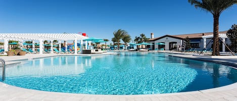 A large outdoor swimming pool with lounge chairs and umbrellas, surrounded by palm trees and a white gazebo.