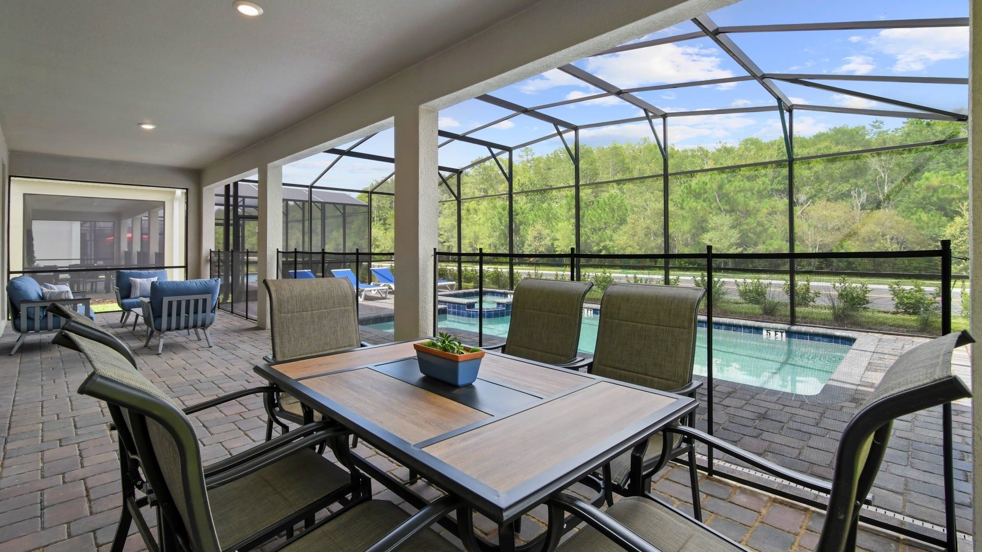 A covered outdoor seating area with a pool view, featuring a table with chairs and a potted plant.